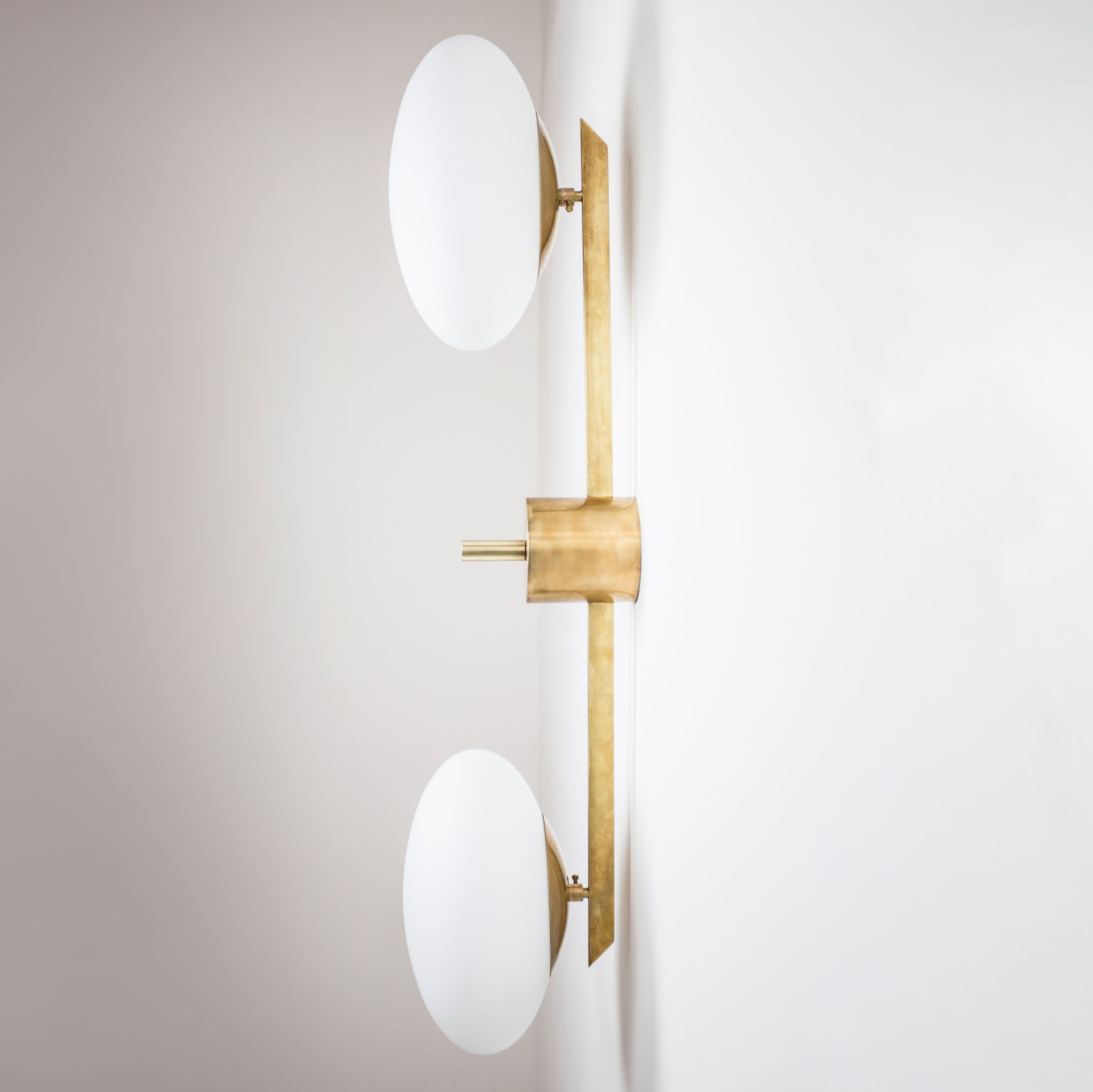 This elegant and iconic lamp in brass and opaline is inspired by mid-century Italian design. Toi&Moi is composed of 2 arms that branch off from a central brass body, supporting with elegant lightness as many Murano opaline glass globes. It can be mounted both as a ceiling and a wall lamp. Angelo Lelli style
