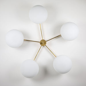 This elegant and iconic lamp in brass and opaline is inspired by mid-century Italian design. Daisy is composed of 5 arms that branch off from a central brass body, supporting with elegant lightness as many Murano opaline glass globes. It can be mounted both as a ceiling and a wall lamp. Angelo Lelli Style