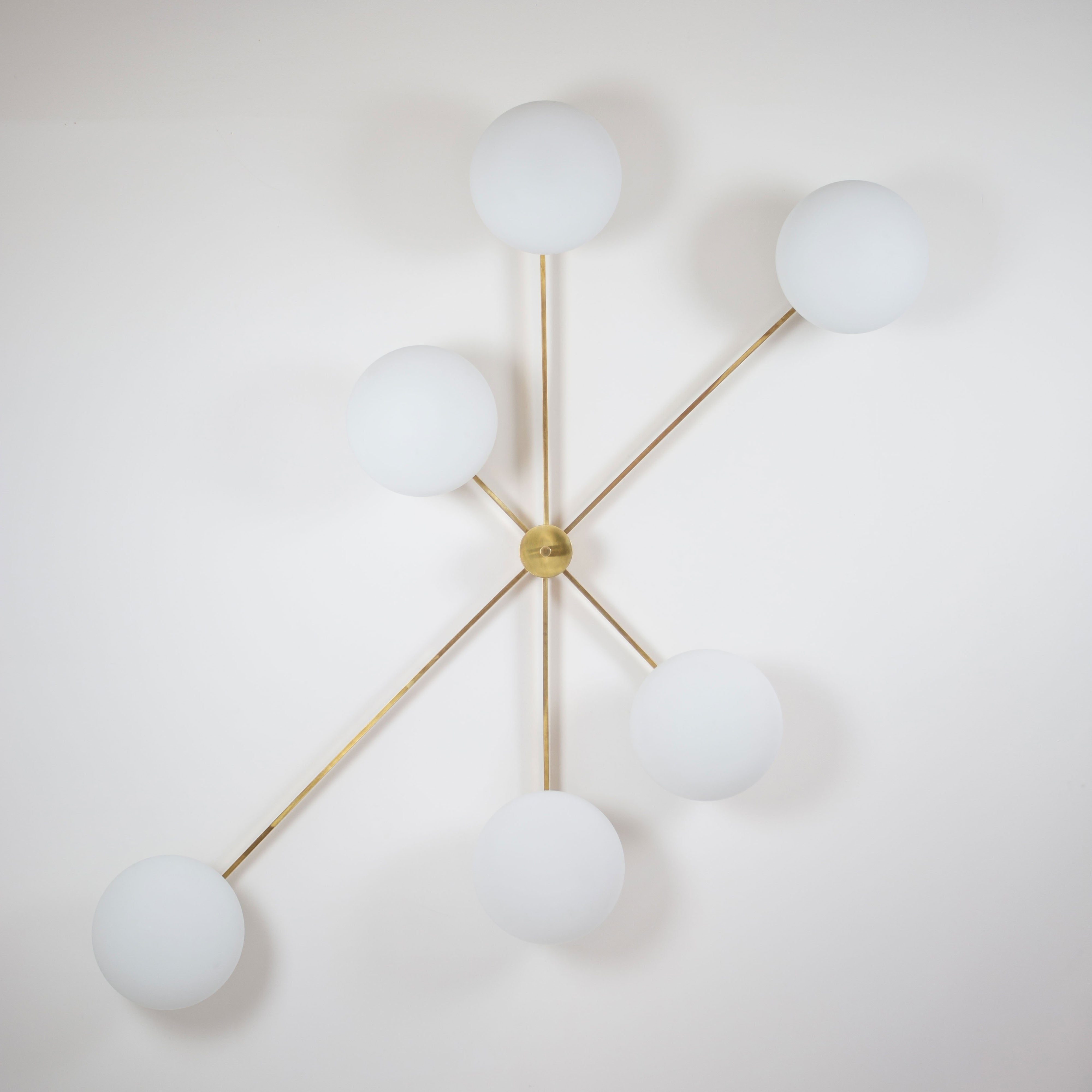 This elegant and iconic lamp in brass and opaline is inspired by mid-century Italian design. Tribute is composed of 6 arms that branch off from a central brass body, supporting with elegant lightness as many Murano opaline glass globes. It can be mounted both as a ceiling and a wall lamp. Angelo Leli style