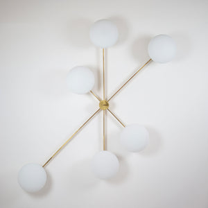 This elegant and iconic lamp in brass and opaline is inspired by mid-century Italian design. Tribute is composed of 6 arms that branch off from a central brass body, supporting with elegant lightness as many Murano opaline glass globes. It can be mounted both as a ceiling and a wall lamp. Angelo Leli style