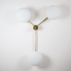 This elegant and iconic lamp in brass and opaline is inspired by mid-century Italian design. Triennale is composed of 3 arms that branch off from a central brass body, supporting with elegant lightness as many Murano opaline glass globes. It can be mounted both as a ceiling and a wall lamp. Angelo Leli style